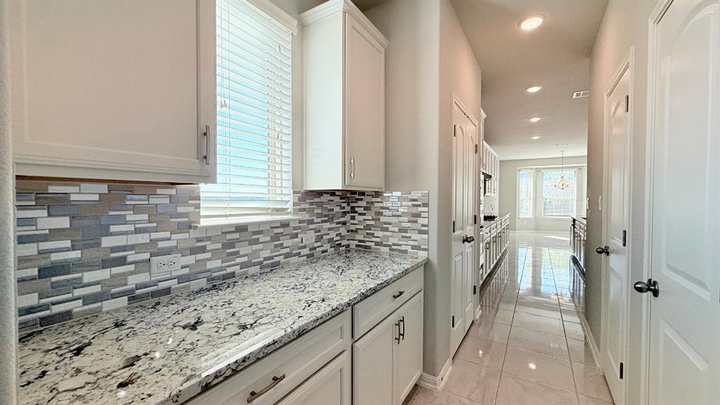 White cabinetry, stone-surface countertops, multi-tonal rectangular tile backsplash, and polished tile flooring