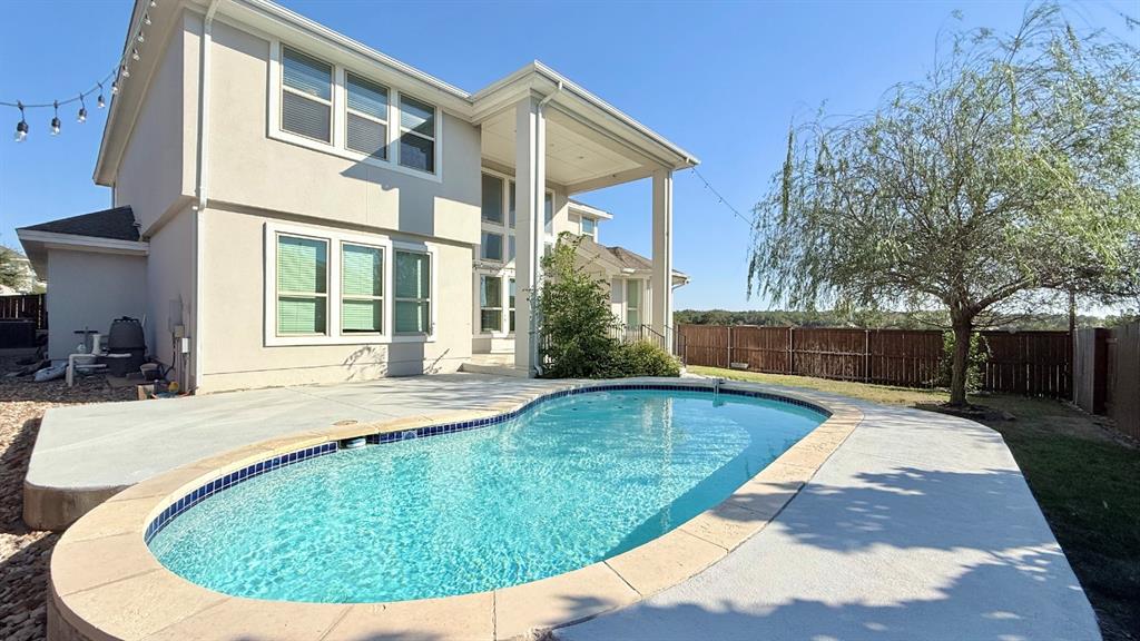 Two-story exterior featuring a stucco finish, a covered rear patio, a swimming pool with stone-style coping, and perimeter wood fencing