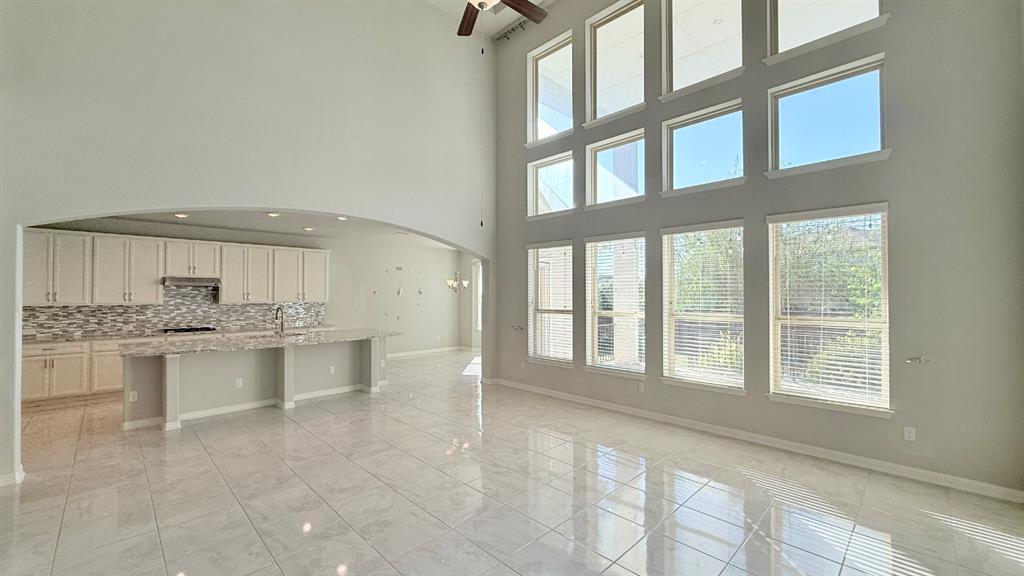 High-ceiling living area featuring a multi-level grid of large windows, tile flooring, arched architectural detailing, and a kitchen island with stone-surface countertops