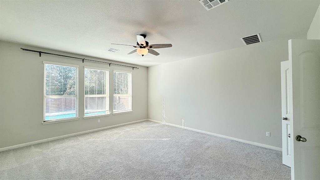 Spacious room featuring neutral carpeting, triple-window configuration with blinds, integrated ceiling fan with light fixture, and arched interior door