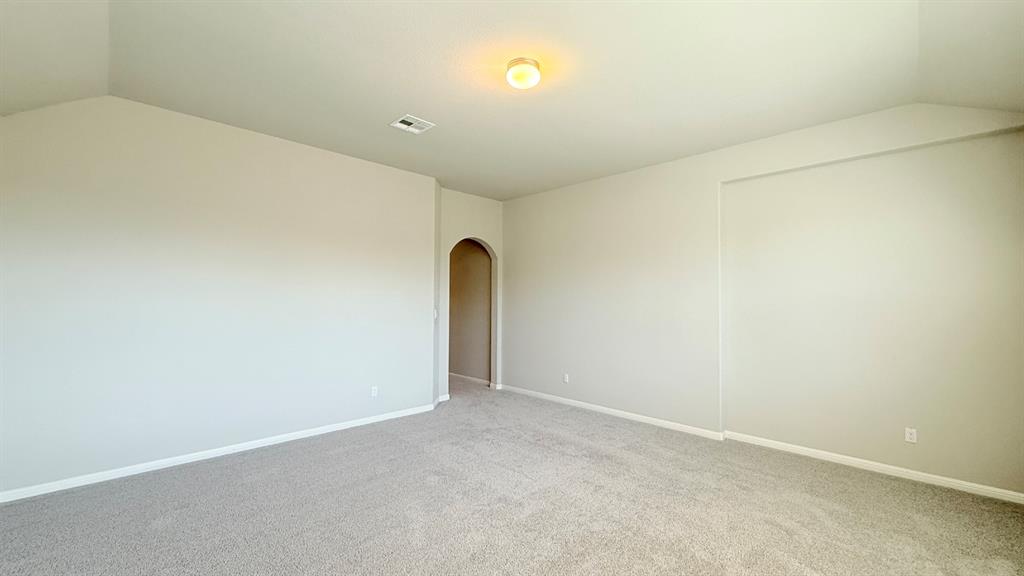 Vaulted ceiling, neutral wall tones, wall-to-wall carpeting, and an arched entryway