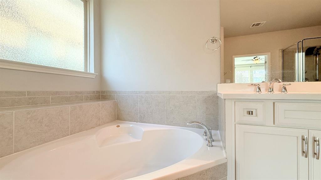Corner soaking tub with tile surround, white cabinetry, integrated countertop, and chrome fixtures