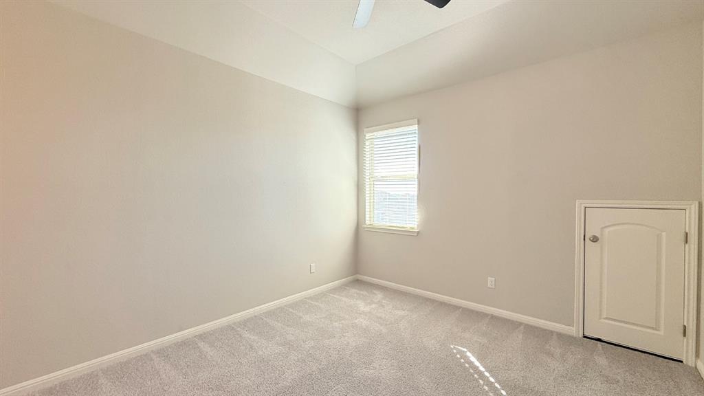 Room featuring a tray ceiling, neutral-toned wall paint, plush carpeting, a single window with blinds, and built-in attic access storage