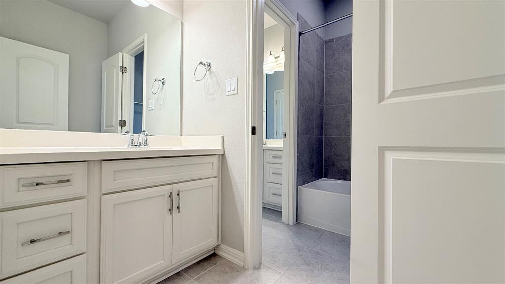 Bathroom featuring white shaker-style cabinetry, a solid surface countertop with an integrated basin, a large wall-mounted mirror, and a tub-shower combination with dark gray tiled surround