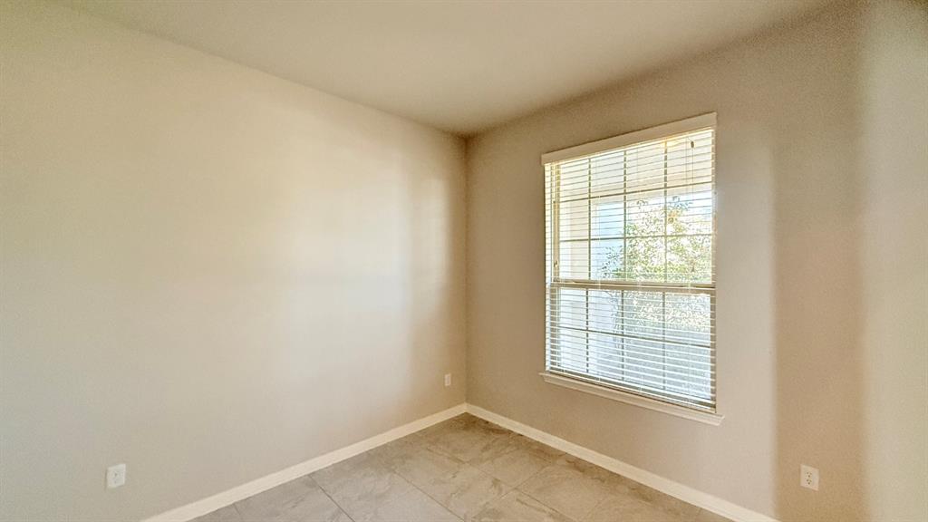 Neutral-toned interior space featuring light-colored wall paint, large-format tile flooring, and a single-hung window with installed horizontal blinds