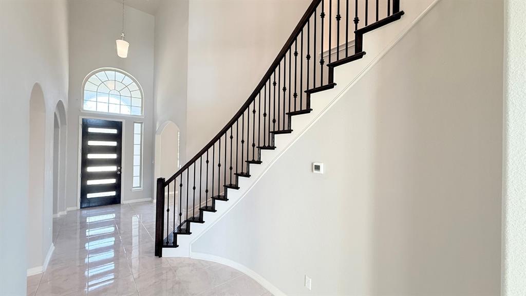 Grand entryway featuring vaulted ceilings, polished tile flooring, a dark-toned front door with horizontal glass panels, a semi-circular transom window, and a staircase with decorative iron balusters