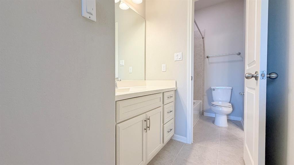 Vanity with stone-finish countertop, undermount sink, shaker-style cabinetry, wall-to-wall mirror, and tile flooring