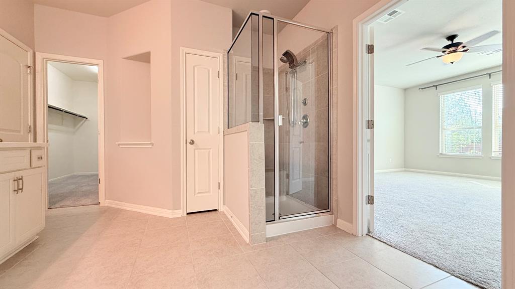 Shower enclosure with tiled surround and multi-head fixture, tile flooring, built-in cabinetry, and walk-in storage area