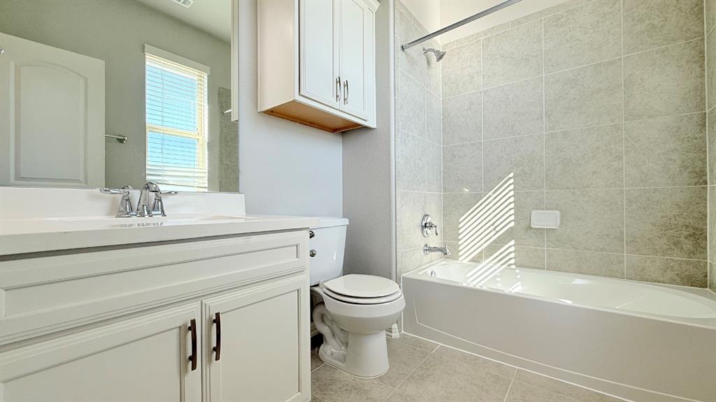 Bathroom featuring a white vanity cabinet with an integrated basin, a wall-mounted medicine cabinet, a tiled shower surround, and a porcelain bathtub