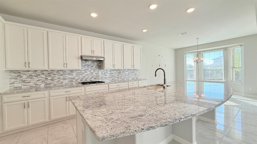 Kitchen featuring white cabinetry, stone countertops, multi-toned tile backsplash, stainless steel range hood, and large central island