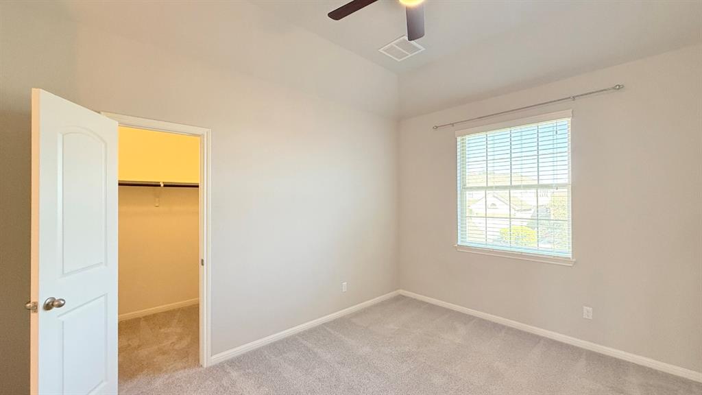 Room featuring high ceilings, wall-to-wall carpeting, a ceiling fan, and a walk-in closet