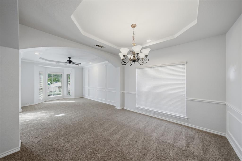 Tray ceiling featuring a decorative chandelier, wainscoting, arched architectural detail, neutral-toned carpeting, and a bay window