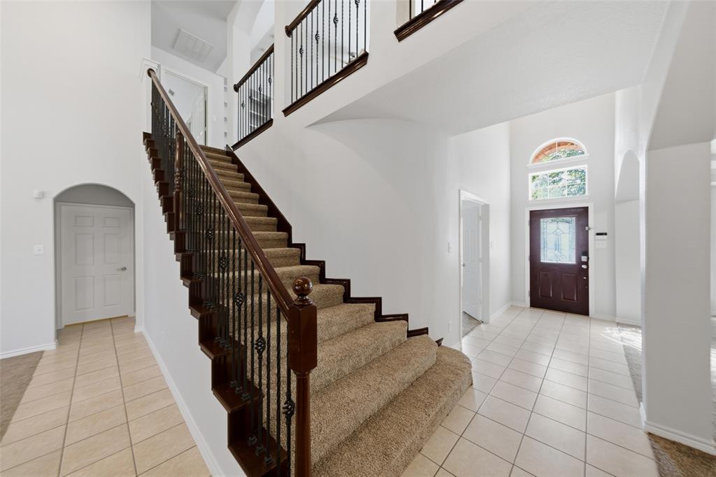Entryway featuring high ceilings, arched architectural detailing, tile flooring, a staircase with a wooden handrail and iron balusters, and a front door with a decorative glass insert