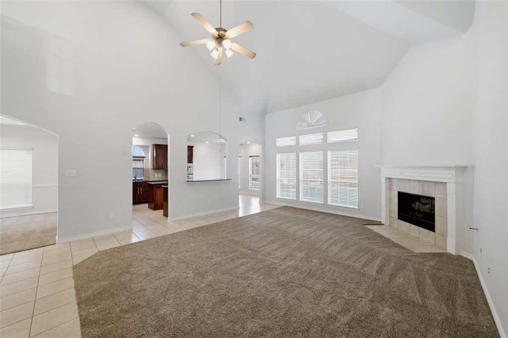 Vaulted ceiling living area featuring a fireplace with a decorative mantel, arched wall openings, multi-pane windows with a fanlight, and a central ceiling fan