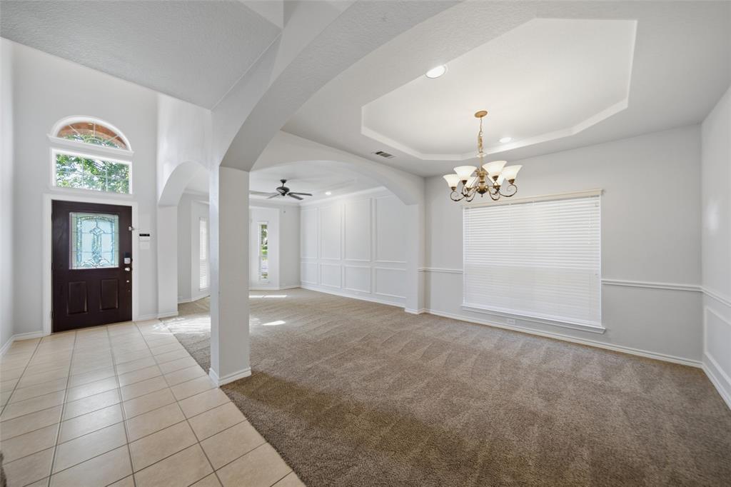 Entry featuring ceramic tile flooring, arched architectural detailing, tray ceiling with multi-arm chandelier, and decorative wall molding