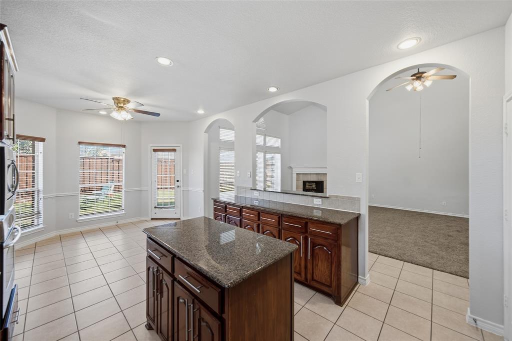 Kitchen featuring an island, stone-finish countertops, wood-finish cabinetry, recessed lighting, and tile flooring