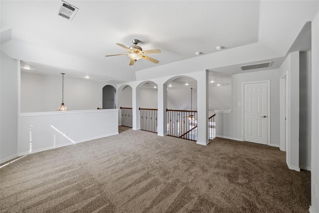 Tray ceiling, metal baluster railings, decorative archways, neutral wall-to-wall carpeting, and a ceiling fan with integrated lighting