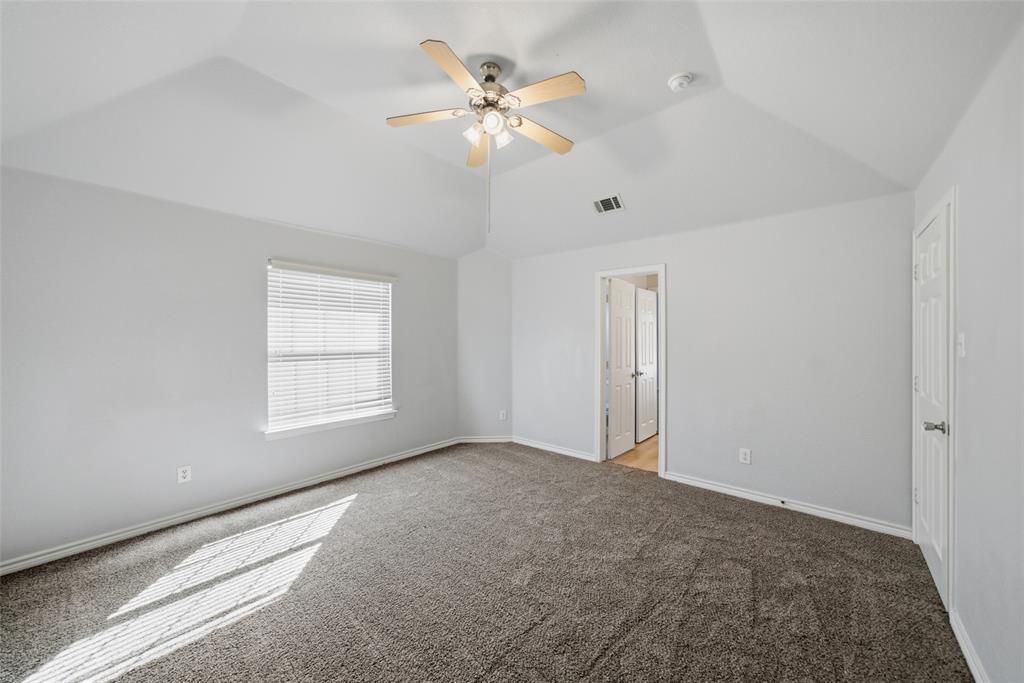 Vaulted ceiling featuring a central lighted ceiling fan, neutral carpeting, and a multi-panel interior door