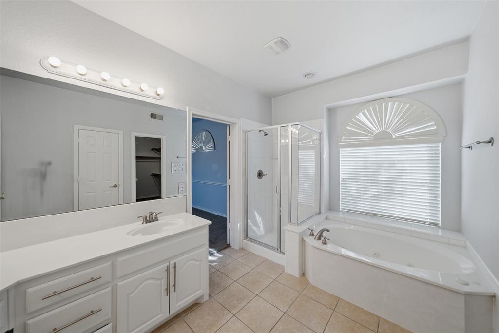 Bathroom featuring a dual-sink vanity with white cabinetry, a walk-in glass-enclosed shower, a jetted soaking tub, and an arched window with louvered shutters