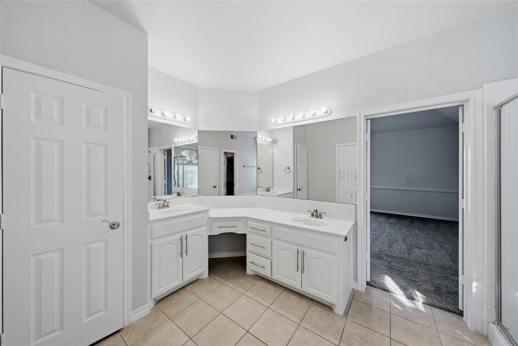Dual-vanity cabinet with integrated makeup counter, white cabinetry, solid-surface countertops, expansive wall-to-wall mirrors, and ceramic tile flooring