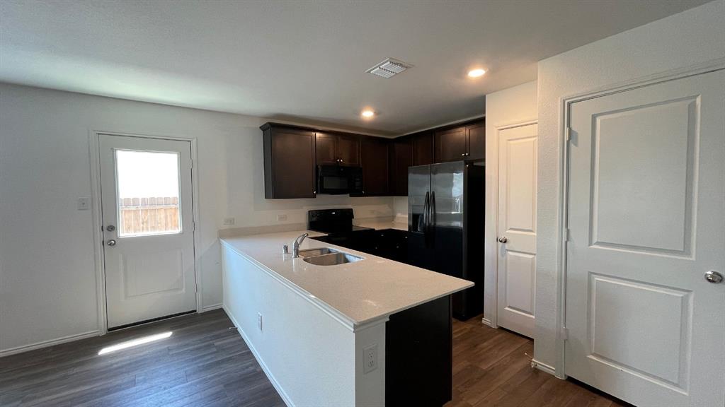 Kitchen featuring dark-finish cabinetry, stone-style countertops, stainless steel sink, integrated appliances, and wood-finish flooring
