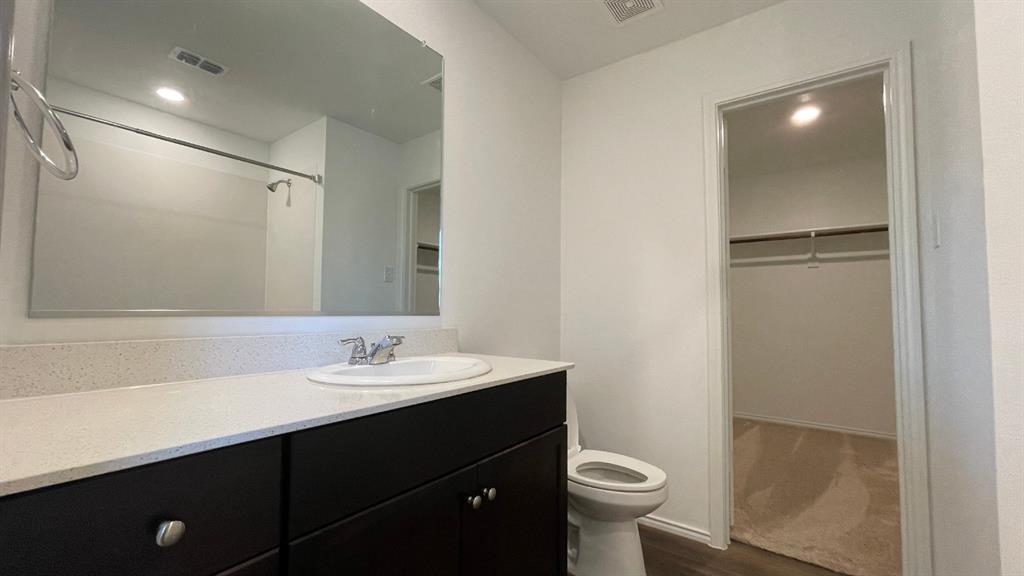 Dark wood-finish cabinetry, light-toned composite countertop with a recessed basin, full-width vanity mirror, and walk-in closet featuring built-in shelving