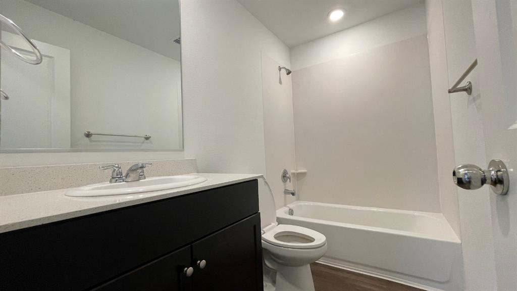 Bathroom featuring a dark wood-finish vanity, light-toned stone countertop with an undermount sink, recessed lighting, and a tub-shower combination with a surround