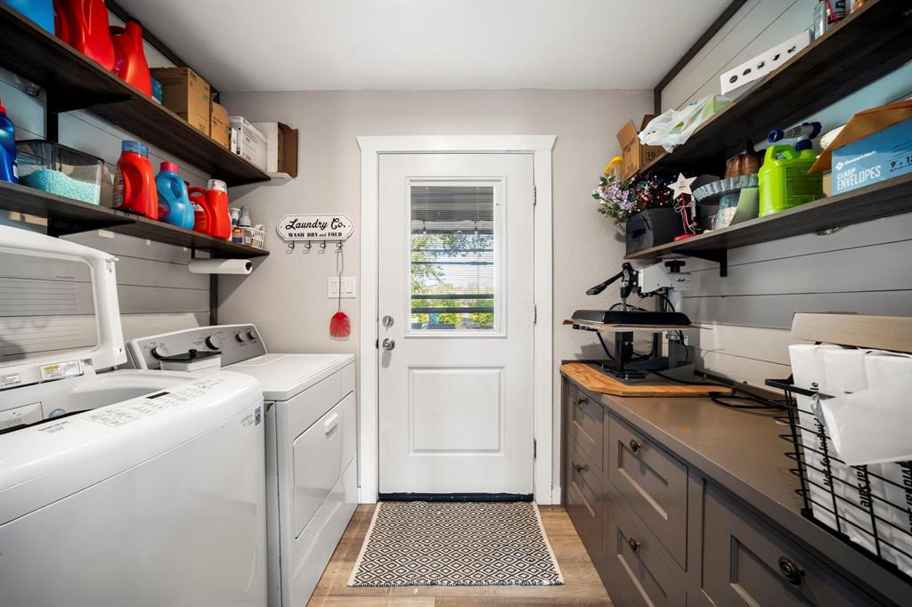 Laundry room featuring shiplap wall paneling, custom gray base cabinetry with a solid surface countertop, open dark wood shelving, and wood-finish flooring