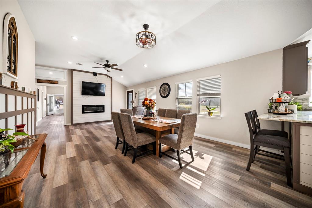 Open-concept living space featuring wood-finish flooring, vaulted ceilings, recessed lighting, horizontal plank accent wall with integrated fireplace, and stone-surfaced kitchen island