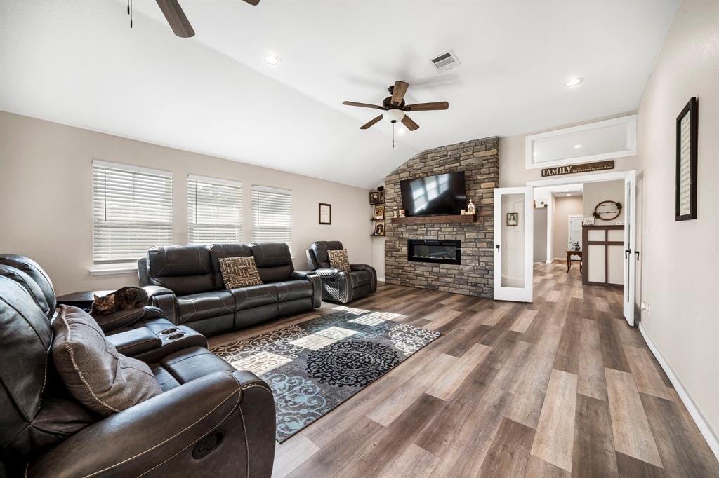 Vaulted ceilings, wood-finish flooring, and a floor-to-ceiling stone fireplace featuring a recessed electric insert and timber mantel