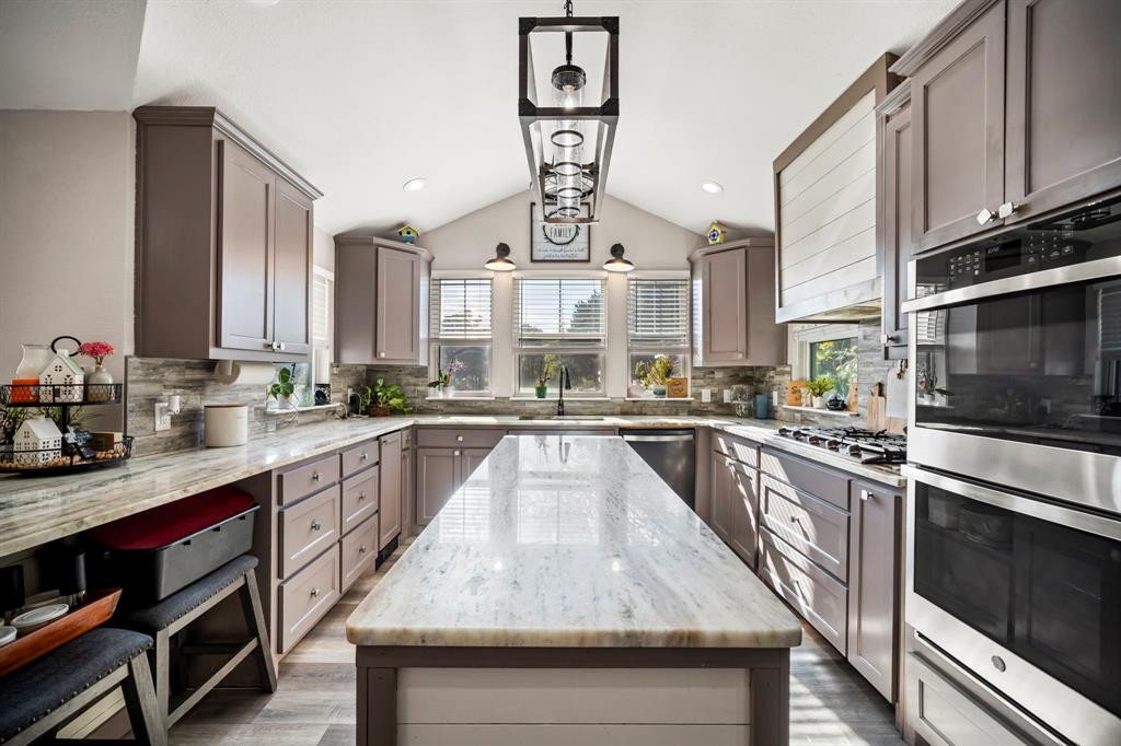 Kitchen featuring custom cabinetry, expansive stone-surface island, vaulted ceiling, stainless steel double wall ovens, and geometric pendant lighting