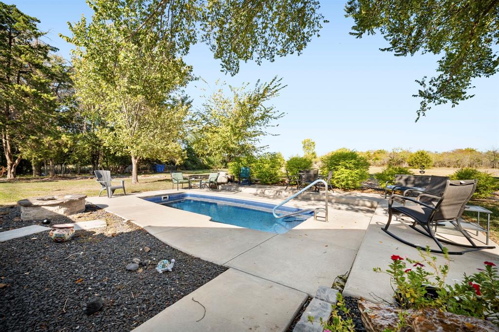 Rectangular in-ground pool with concrete surround, stone fire pit, and mature trees