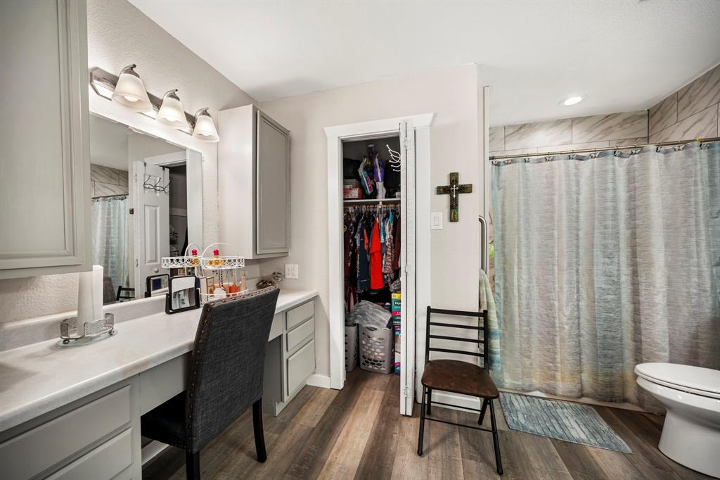 Bathroom featuring wood-finish flooring, built-in vanity with cabinetry, vanity mirror with overhead lighting, closet, and a shower with tiled surround