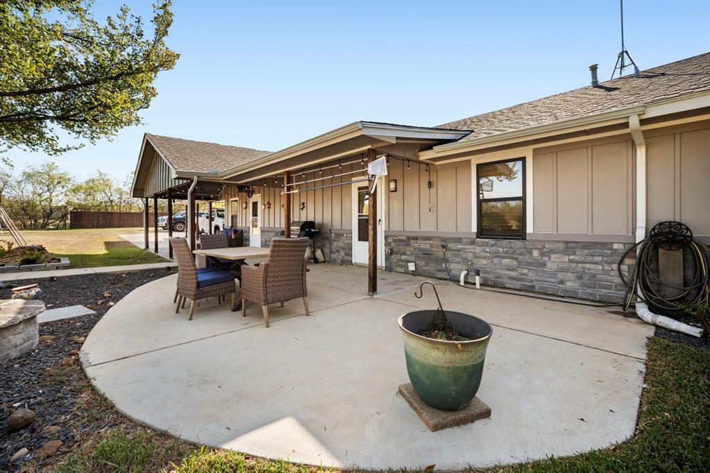Covered concrete patio featuring vertical siding, stone veneer accents, and an attached carport