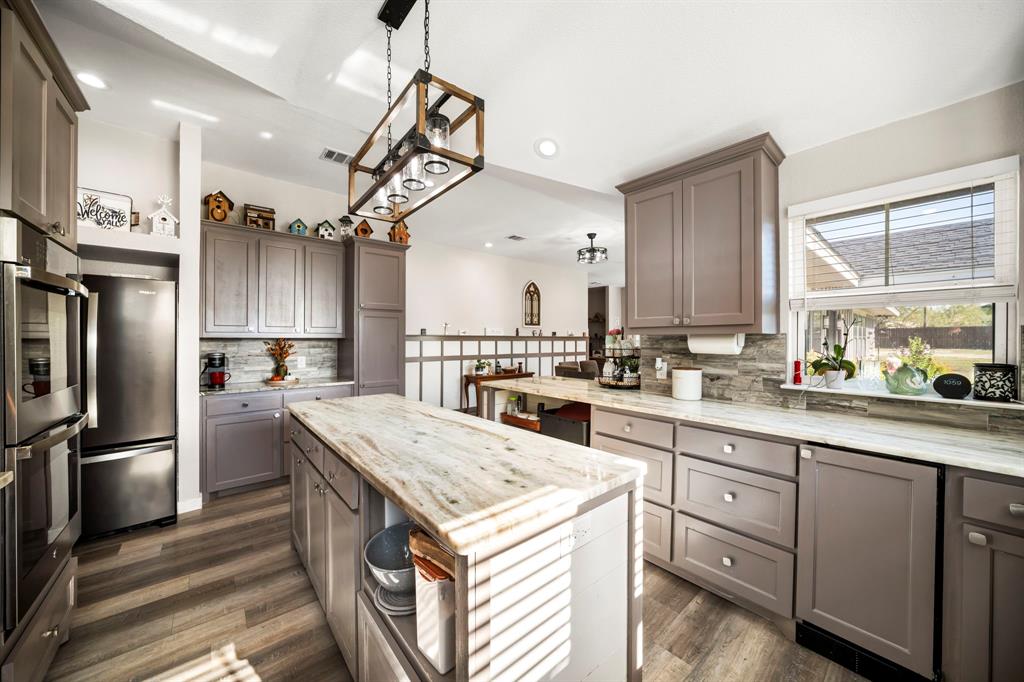 Kitchen featuring grey shaker-style cabinetry, stone-finish countertops, stone tile backsplash, wood-finish flooring, and a rectangular pendant light fixture