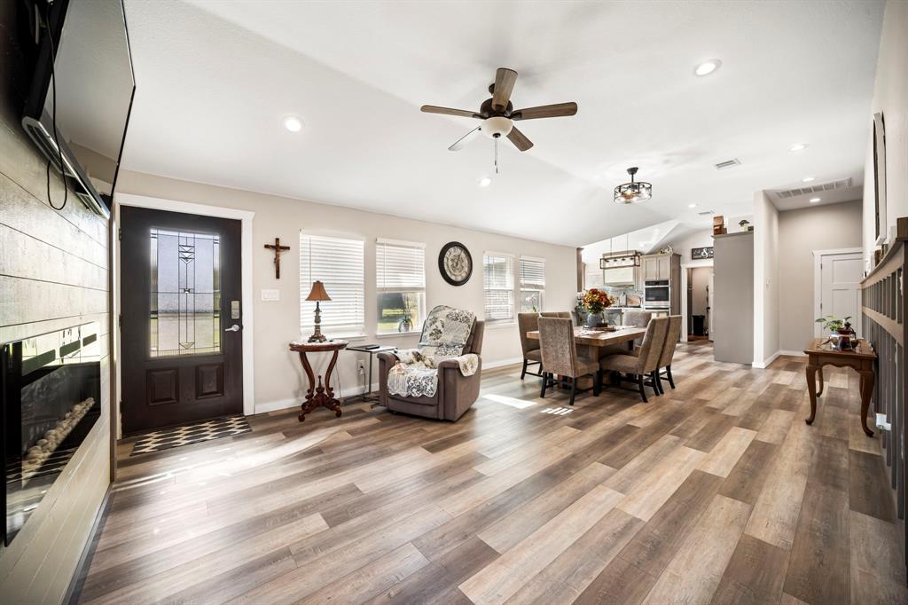 Open-concept area featuring wood-finish flooring, a wall-mounted electric fireplace, vaulted ceiling, recessed lighting, and a fron
