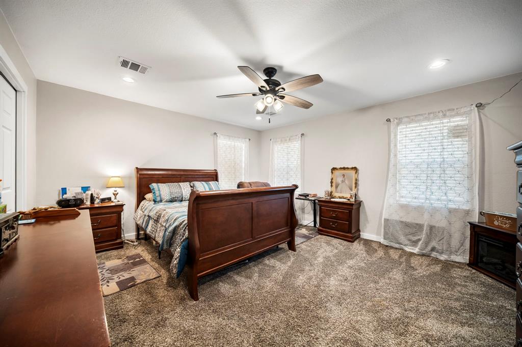 Neutral-toned bedroom featuring carpeting, multi-window configuration, and a central ceiling fan with integrated lighting