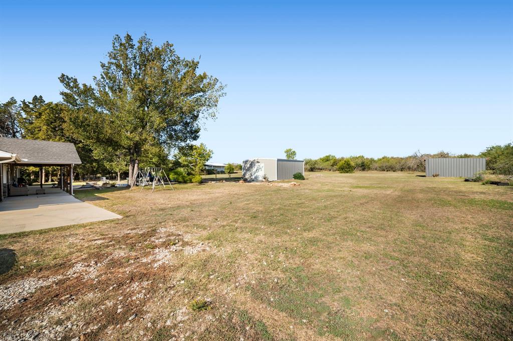 Expansive grounds featuring a concrete patio, mature trees, two exterior storage buildings, and natural landscape