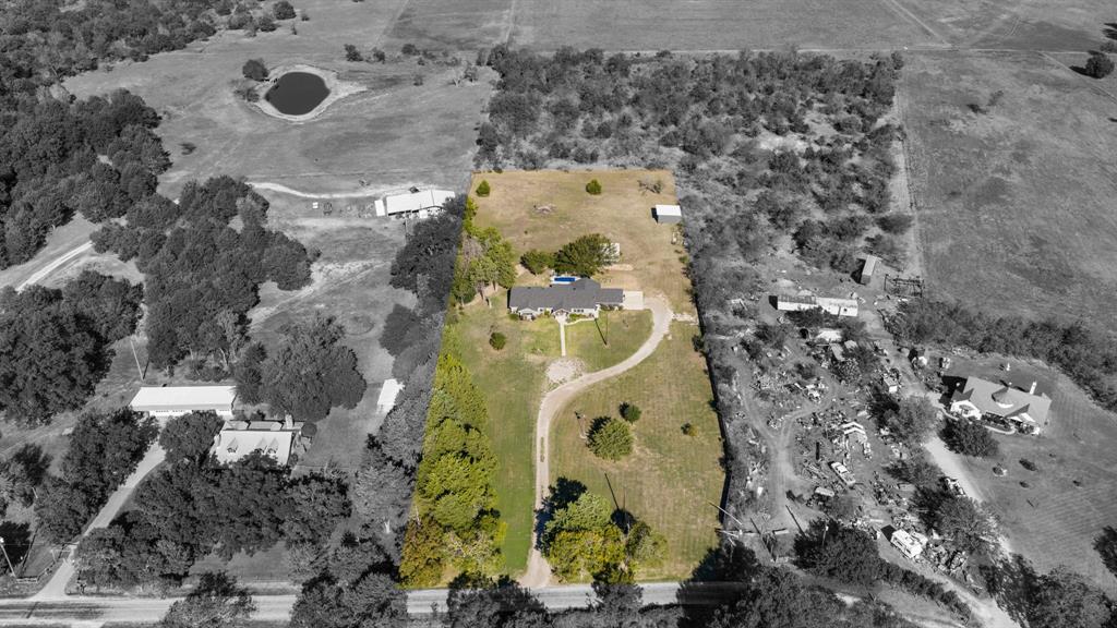 Aerial view of a sprawling property featuring a paved curved driveway, open acreage, mature trees, and an established residential building