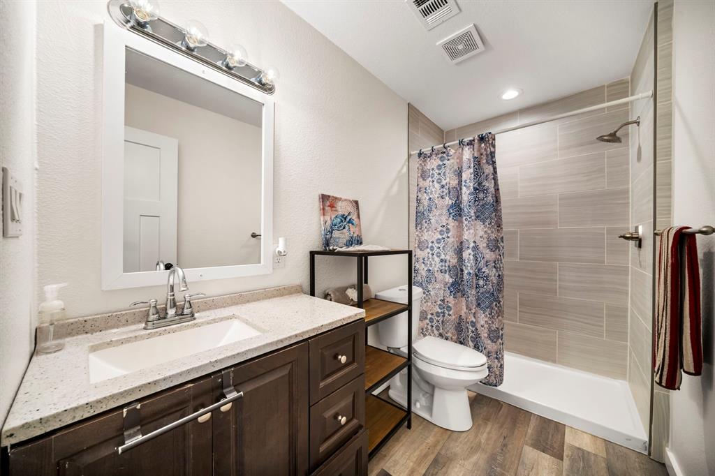 Bathroom featuring a vanity with a light-toned countertop, framed wall mirror, wood-finish flooring, and a walk-in shower with horizontal tile surround
