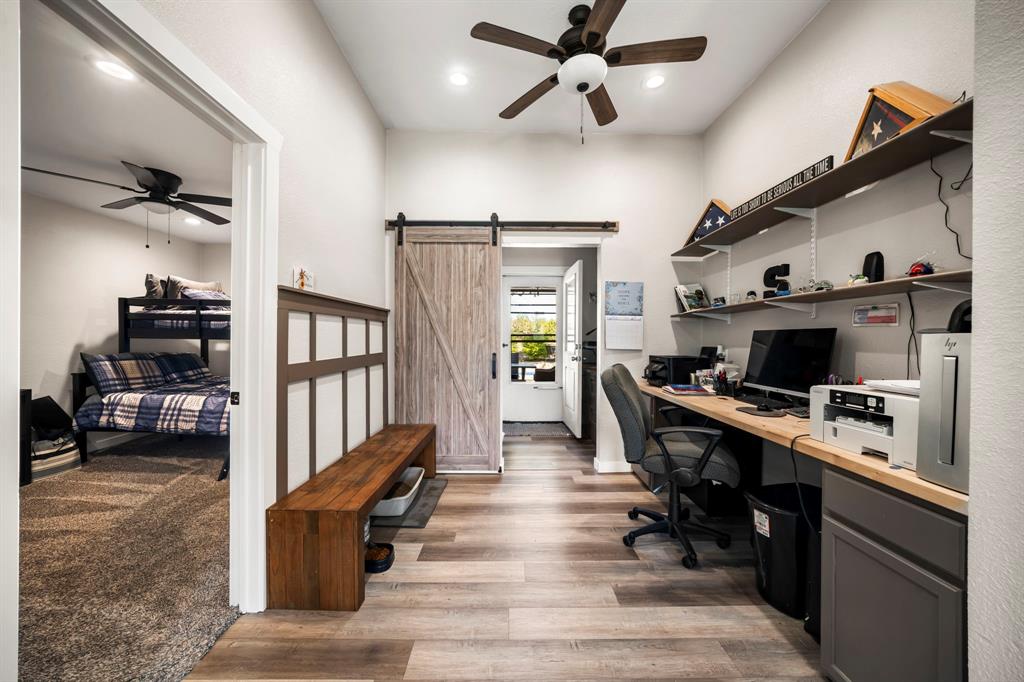 Interior space featuring wood-finish flooring, a rustic barn-style sliding door, built-in wooden desk cabinetry, wall-mounted shelving, and a decorative wood wainscot panel with a bench