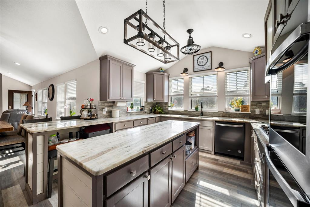 Kitchen featuring a central island with stone-finish countertops, shaker-style cabinetry, a geometric pendant light fixture, and wood-finish flooring