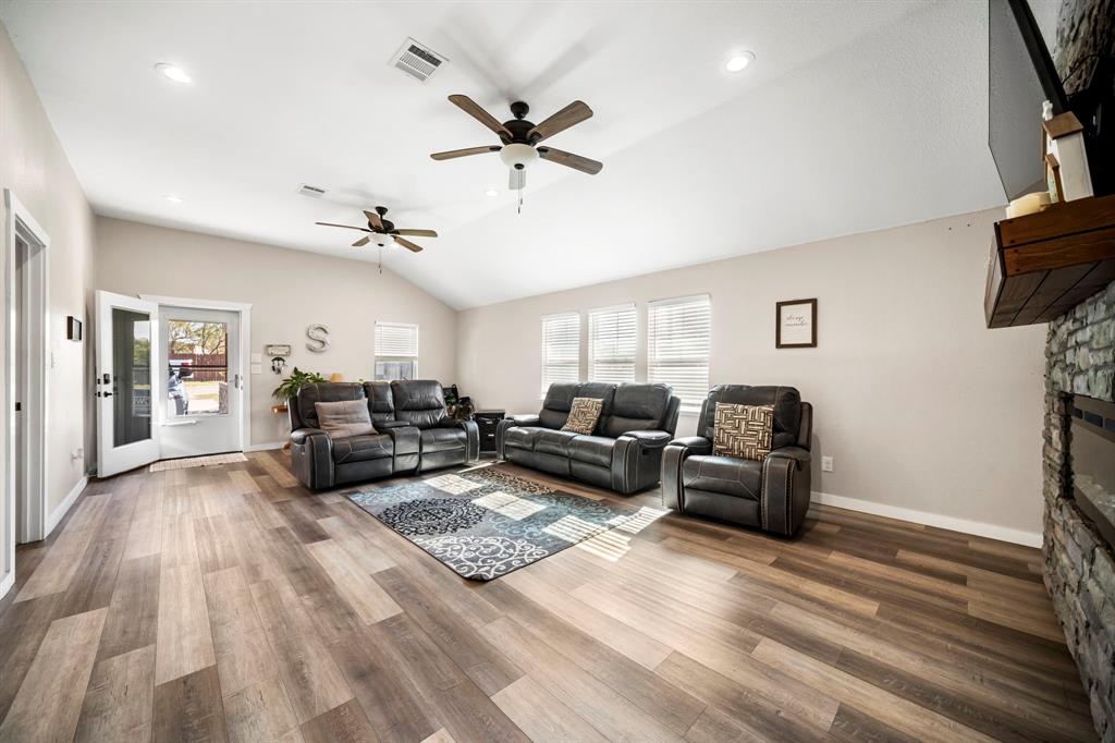 Vaulted ceilings, wood-finish flooring, dual ceiling fans, recessed lighting, and a stone-faced fireplace with a wooden mantel