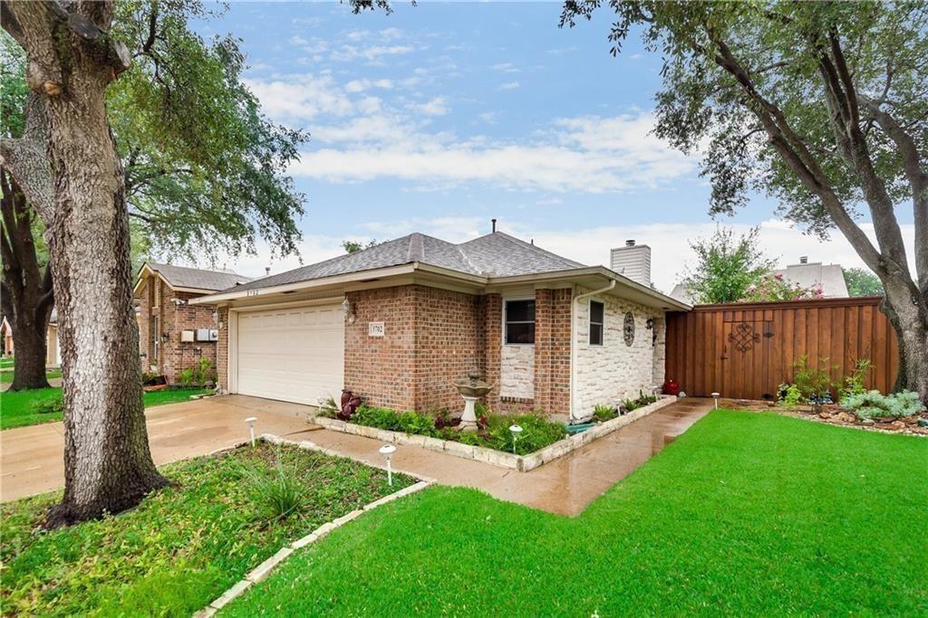 Single-story exterior featuring a brick and stone facade, hip roof, two-car garage, and wood privacy fencing
