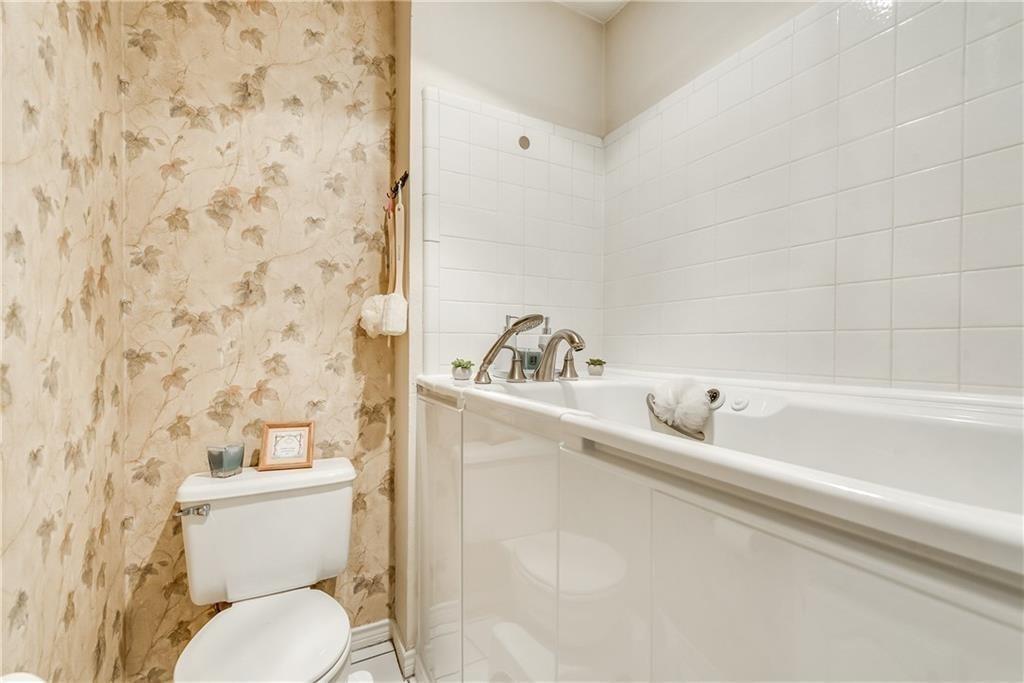 Built-in soaking tub with metallic faucet fixtures, white subway-style tile surround, and dual-flush toilet