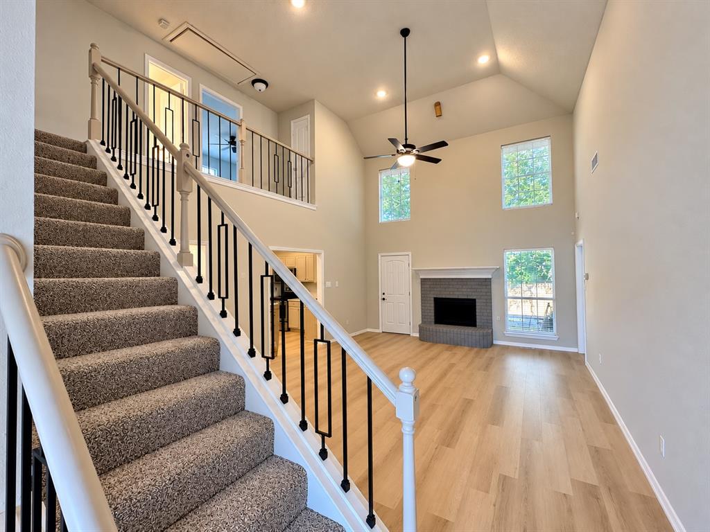 Vaulted ceilings with exposed stairwell, wood-finish flooring, masonry fireplace with raised hearth, and wrought iron baluster railing