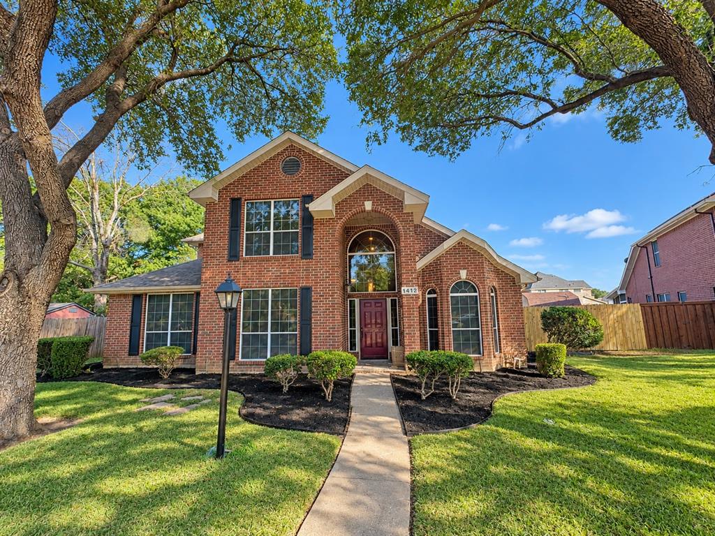 Two-story brick exterior featuring a covered entryway, decorative arched windows, dark window shutters, and a concrete front walkway