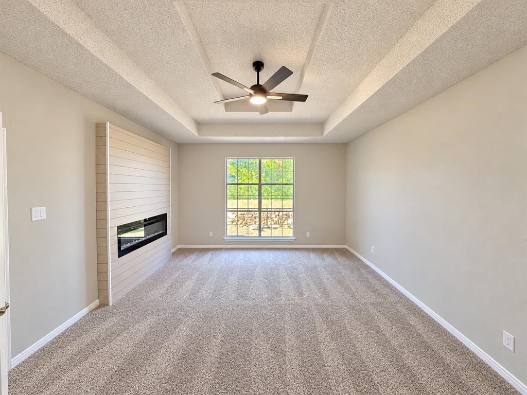 Tray ceiling featuring a central lighted ceiling fan, complemented by a horizontal shiplap fireplace surround and a wall-mounted linear electric fireplace