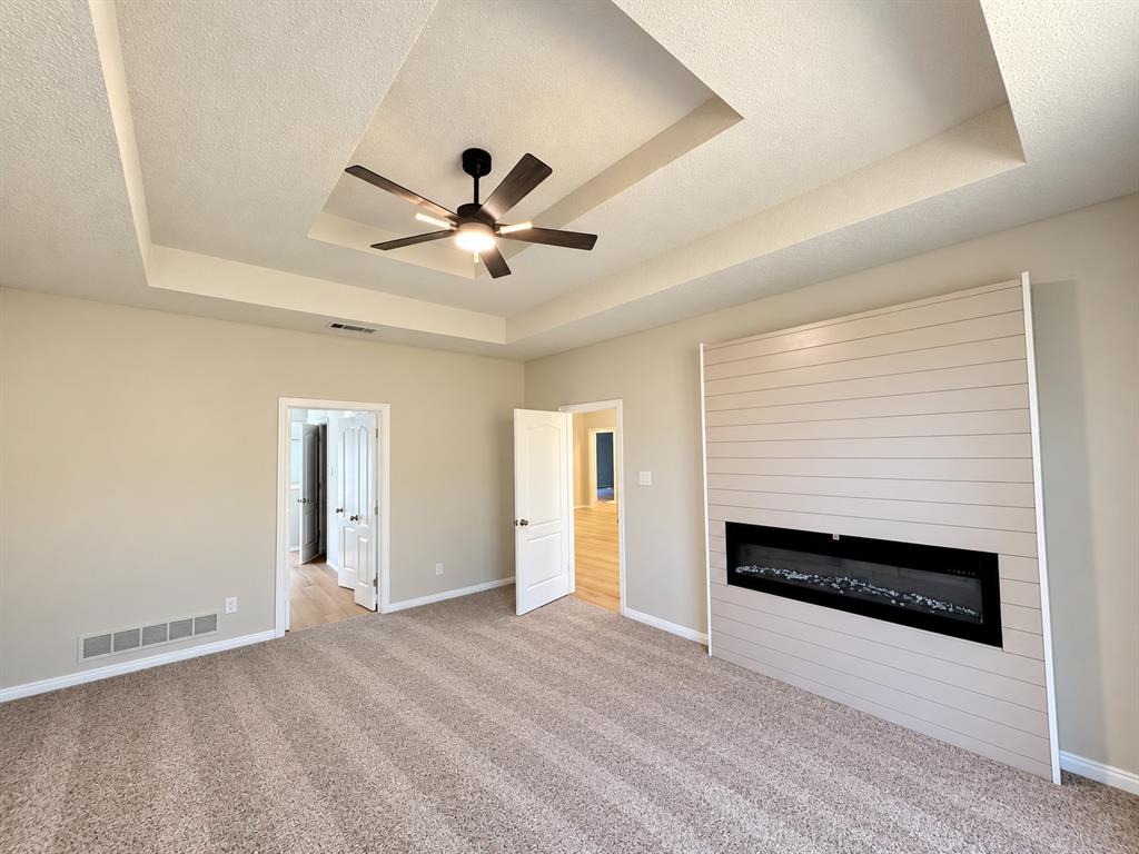 Tray ceiling with a central multi-blade ceiling fan, expansive shiplap accent wall, and integrated horizontal electric fireplace