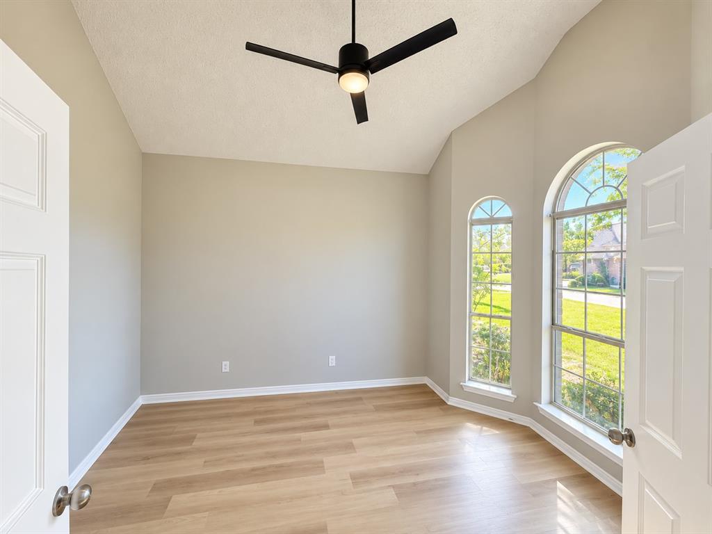 Vaulted ceilings, wood-finish flooring, matte black ceiling fan with integrated lighting, and dual arched windows
